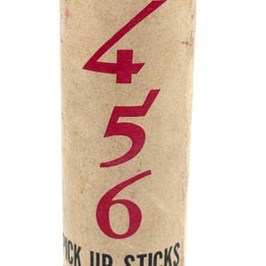 May include: A vintage tube of "Pick Up Sticks" game. The cylindrical container is tan with red text and numbers. The numbers "456" are prominently displayed. The text "ORIGINAL" is at the top, and "PICK UP STICKS" and "PHILADELPHIA, PA" are at the bottom.