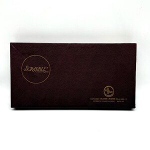 May include: A brown box with the words "SCRABBLE® the crossword game" in gold lettering. The box also has a gold seal with the words "SELCHOW & RIGHTER CO.  BAY SHORE, N.Y.  THE PRODUCTION AND ADVERTISING COMPANY  MADE IN U.S.A."