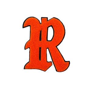 May include: A bright orange letter R patch featuring a textured surface and a bold black outline. The letter is designed in a stylized gothic font with sharp serifs and distinct curves, creating a high-contrast graphic element for apparel.
