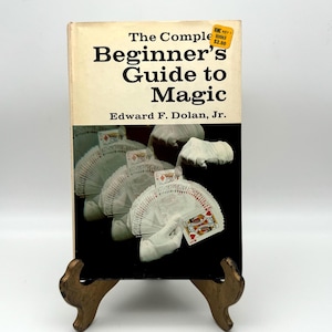 May include: A vintage book titled "The Complete Beginner's Guide to Magic" by Edward F. Dolan, Jr. The book cover features a close-up of a hand performing a magic trick with a deck of cards.