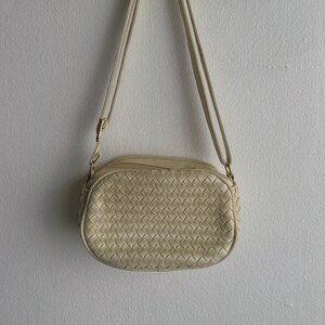 May include: A cream-colored woven leather crossbody bag with a long strap.