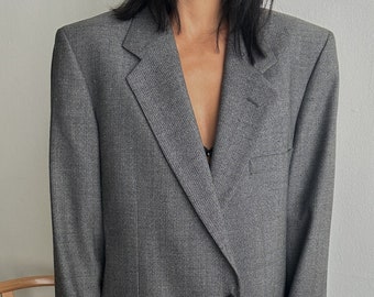 Puede incluir: Una chaqueta gris con un cierre de un botón. La chaqueta tiene un corte largo y relajado y una silueta ligeramente oversized.