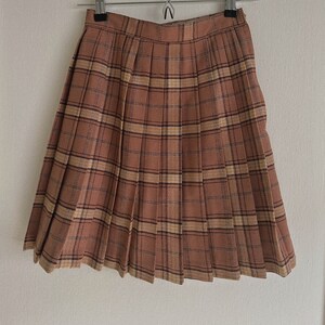 May include: A brown plaid pleated skirt with a black waistband. The skirt is hanging on a hanger.