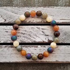 May include: A beaded bracelet with a variety of colors, including brown, orange, yellow, and iridescent blue. The beads are round and smooth, and the bracelet is strung on a clear elastic cord.