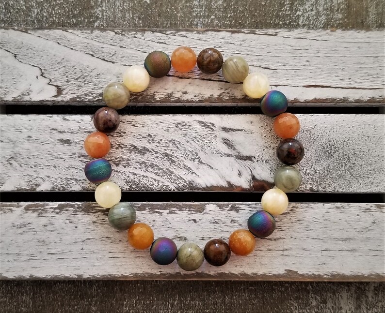 May include: A beaded bracelet with a variety of colors, including brown, orange, yellow, and iridescent blue. The beads are round and smooth, and the bracelet is strung on a clear elastic cord.