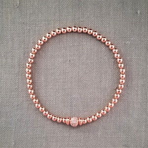 May include: A rose gold beaded bracelet with a small, sparkly rose gold charm.