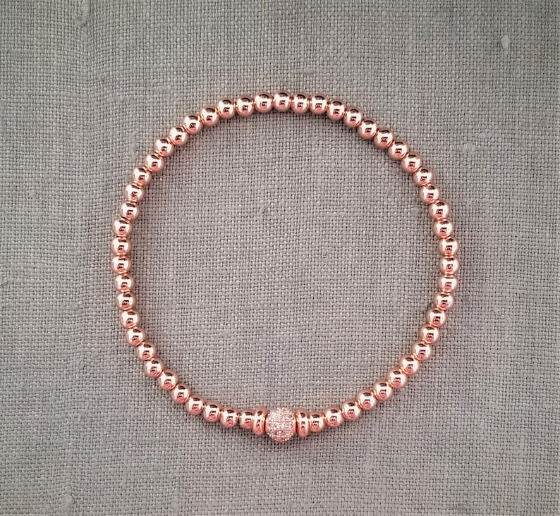 May include: A rose gold beaded bracelet with a small, sparkly rose gold charm.