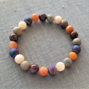 May include: A beaded bracelet with a variety of colors, including orange, brown, gray, and iridescent blue. The beads are round and smooth.