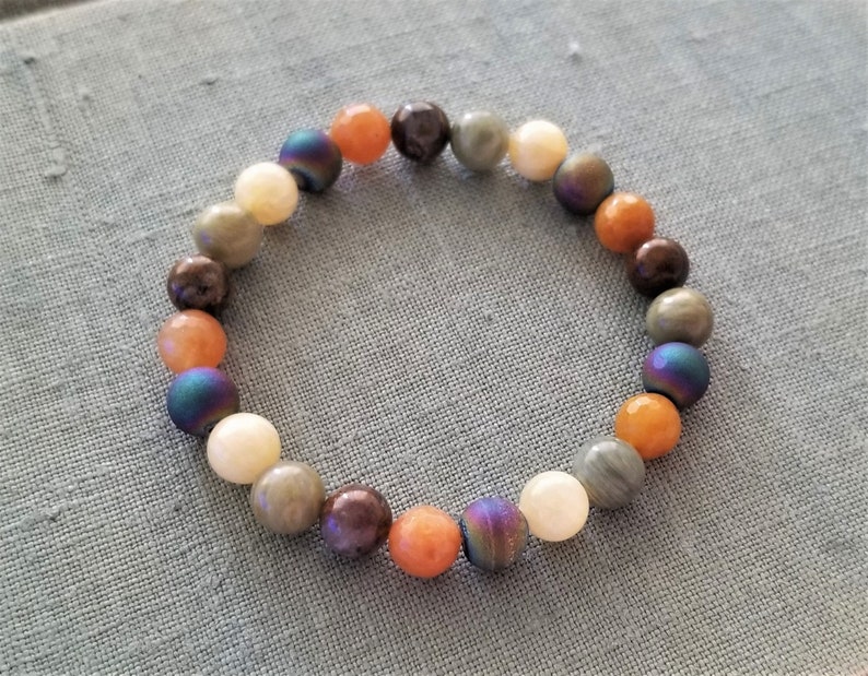 May include: A beaded bracelet with a variety of colors, including orange, brown, gray, and iridescent blue. The beads are round and smooth.