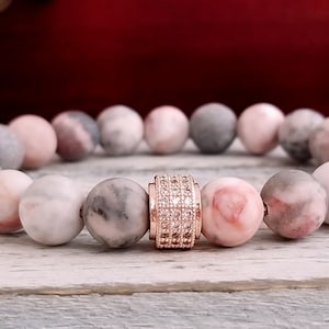 May include: A bracelet made of pink and gray marbled beads with a rose gold accent bead featuring clear rhinestones.