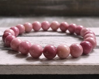 Puede incluir: Un brazalete de piedras preciosas rosas hecho de cuentas redondas. El brazalete está hecho de piedras naturales y es una pieza de joyería hermosa y única.
