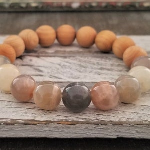 Può includere: Un braccialetto di perline con perline di legno e pietra. Il braccialetto presenta un design circolare con perline di legno marrone chiaro e una varietà di perline di pietra nei toni del beige, grigio e marrone.