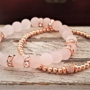 May include: Two bracelets, one with rose gold beads and a crystal accent, and the other with larger rose quartz beads with crystal accents.
