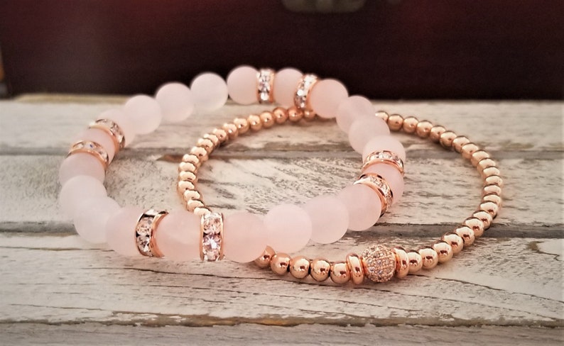 May include: Two bracelets, one with rose gold beads and a crystal accent, and the other with larger rose quartz beads with crystal accents.