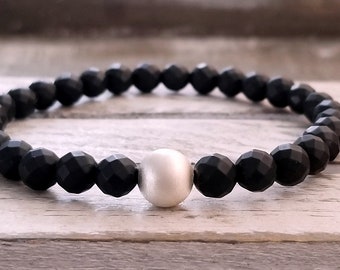 Puede incluir: Un brazalete de cuentas negras con una sola cuenta blanca en el centro.