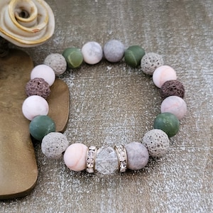 May include: A bracelet made of brown, gray, and green lava rock beads with a clear crystal bead in the center.