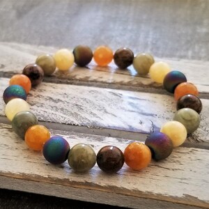 May include: A bracelet made of various colored stones, including green, brown, yellow, and orange. The stones are round and have a smooth finish.