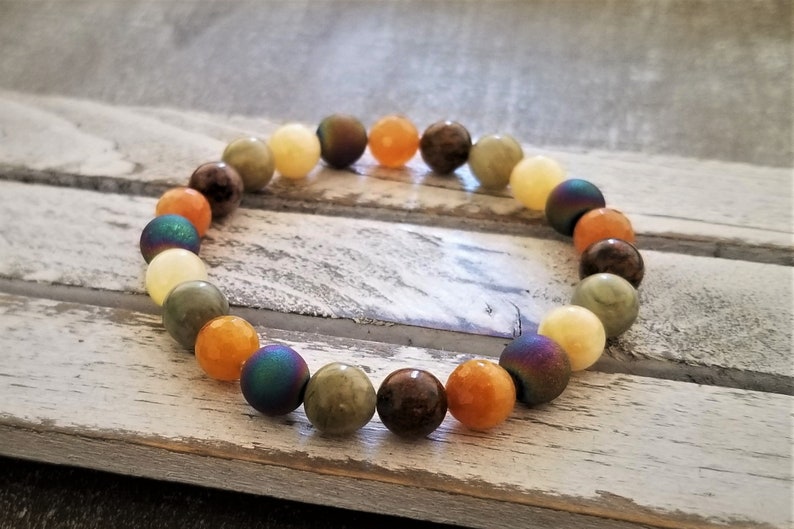 May include: A bracelet made of various colored stones, including green, brown, yellow, and orange. The stones are round and have a smooth finish.
