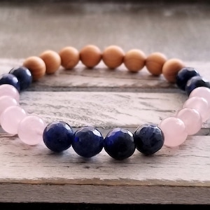 Puede incluir: Un brazalete hecho con cuentas rosas, azules y marrones. El brazalete está hecho con piedras naturales y madera.