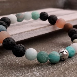 May include: A beaded bracelet with black lava rock, light blue and green stones, and a silver spacer bead.