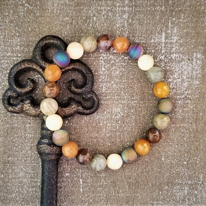May include: A beaded bracelet with a variety of colors and textures, including brown, white, orange, and iridescent blue. The bracelet is lying on a wooden surface.