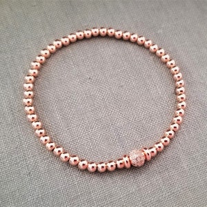 May include: A rose gold beaded bracelet with a small rose gold bead with clear crystals in the center.