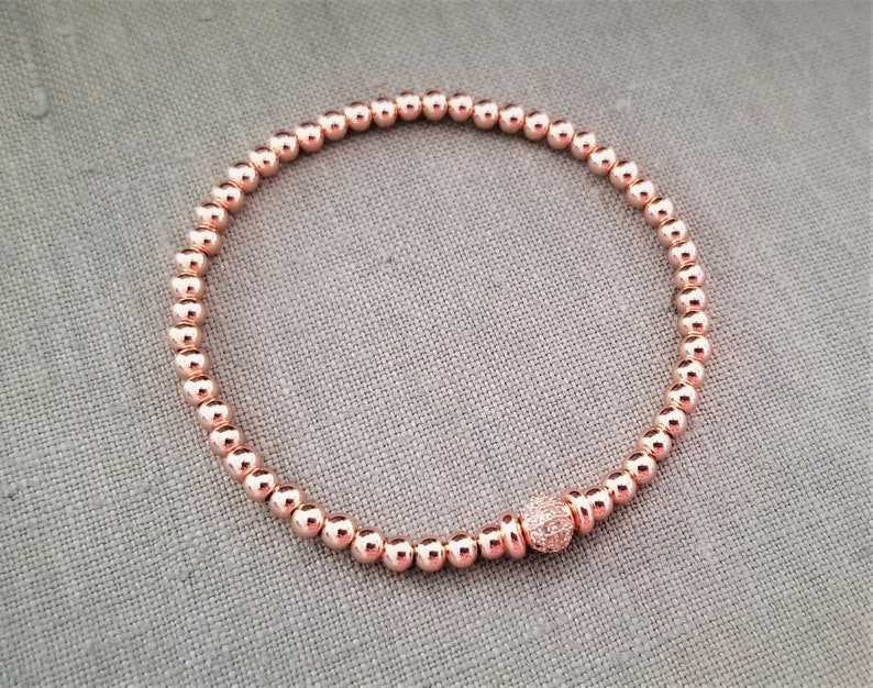 May include: A rose gold beaded bracelet with a small rose gold bead with clear crystals in the center.