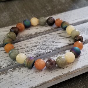 May include: A bracelet made of various colored gemstone beads, including green, brown, orange, and iridescent blue. The beads are strung on a clear elastic cord.