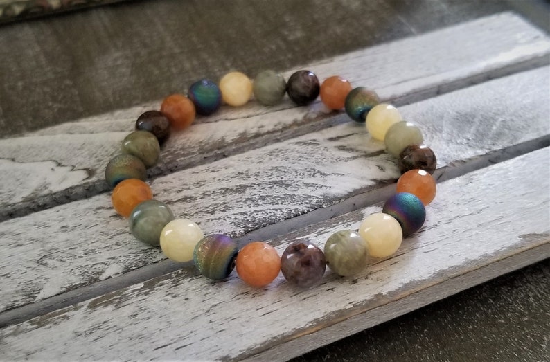 May include: A bracelet made of various colored gemstone beads, including green, brown, orange, and iridescent blue. The beads are strung on a clear elastic cord.