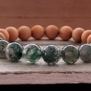 May include: A green moss agate and sandalwood beaded bracelet. The bracelet is made with alternating green moss agate and sandalwood beads.