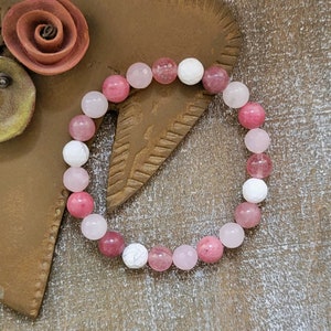 May include: A pink and white gemstone bracelet with round beads. The bracelet is made of natural stones and is a beautiful accessory for any occasion.