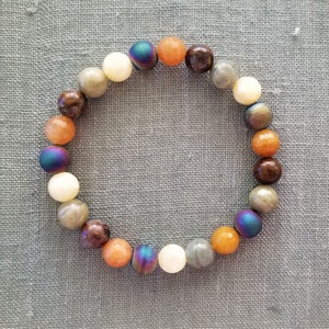 May include: A beaded bracelet with a variety of colors, including brown, orange, white, and iridescent blue. The beads are round and smooth.