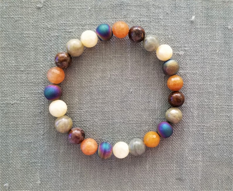 May include: A beaded bracelet with a variety of colors, including brown, orange, white, and iridescent blue. The beads are round and smooth.
