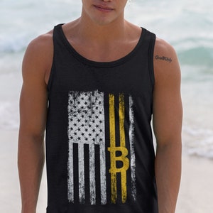 May include: Black tank top featuring a distressed American flag design with a yellow Bitcoin symbol. The flag has white stars and stripes, with a yellow stripe and Bitcoin symbol replacing a traditional stripe. The tank top is sleeveless.