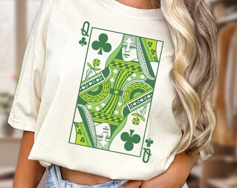 May include: A white t-shirt with a green and yellow graphic of the Queen of Clubs playing card. The card features a clover design and the text "Q of Clubs".