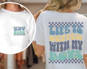 May include: White t-shirt with the text "BOY MAMA" on the front pocket and "LIFE IS BETTER WITH MY BOYS" on the back. The text is in a retro font with blue, yellow, and teal accents, set against a checkered background.