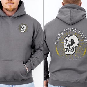 May include: Gray hooded sweatshirt with a white skull graphic on the front and the text "EVERYTHING HURTS AND I'M HUNGRY" on the back.