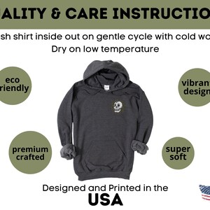 May include: A dark gray hooded sweatshirt with a white skull design on the front. The sweatshirt is made from eco-friendly materials and is super soft. It is designed and printed in the USA.