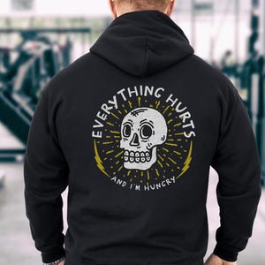 May include: Black hooded sweatshirt with a white skull graphic and the text "Everything Hurts and I'm Hungry".