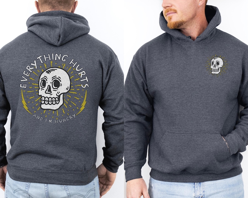May include: A dark gray hooded sweatshirt with a skull graphic and the text "EVERYTHING HURTS AND I'M  HUNGRY" on the back. The front of the sweatshirt has a smaller skull graphic on the chest.