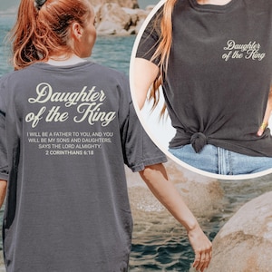May include: A gray t-shirt with the text "Daughter of the King" in white lettering. The shirt also includes a Bible verse: "I will be a father to you, and you will be my sons and daughters, says the Lord Almighty. 2 Corinthians 6:18"