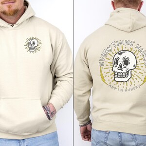 May include: A beige hoodie with a skull graphic on the front and the text "EVERYTHING HURTS AND I'M HUNGRY" on the back.