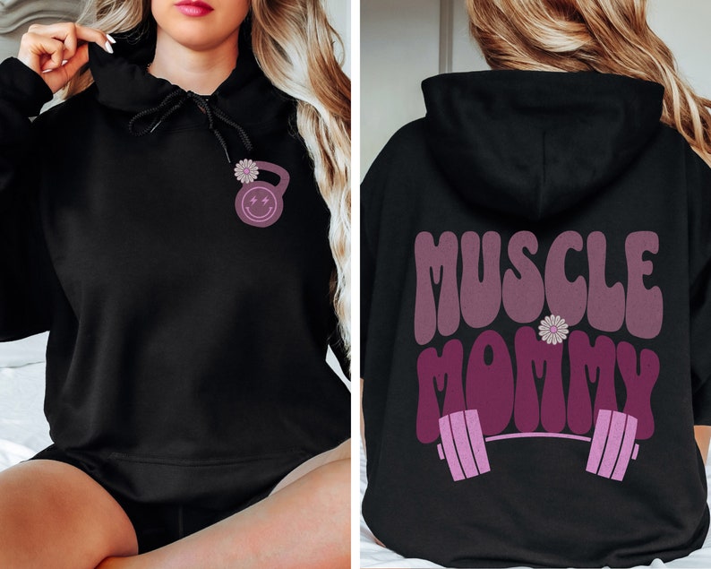 May include: Black hooded sweatshirt with a pink and white flower and a pink dumbbell with a smiley face on the front. The back of the sweatshirt has the text "MUSCLE MOMMY" in pink with a pink barbell and a pink flower.