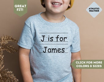 May include: A gray t-shirt with the text "J is for James" printed on it. The shirt is a basic style with a crew neck and short sleeves.