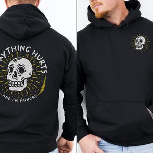 May include: Black hoodie with a white skull graphic on the front and the text "Everything Hurts and I'm Hungry" on the back.