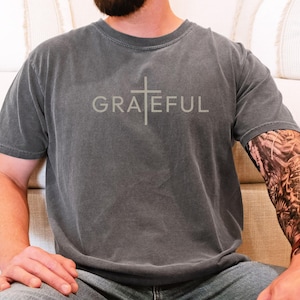 May include: A charcoal gray t-shirt with a white cross and the word "GRATEFUL" printed on the front.