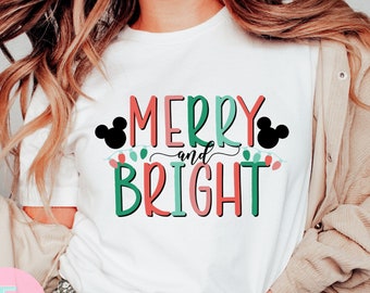 May include: White t-shirt with a red, green, and pink graphic that says "Merry and Bright" with Mickey Mouse ears on either side of the text.