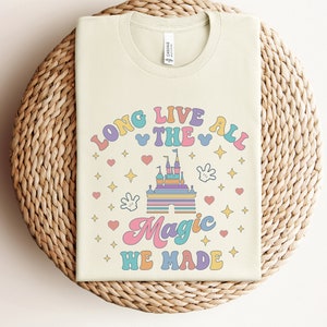 May include: A light beige t-shirt with a colorful graphic design that says "Long Live The All Magic We Made". The graphic includes a cartoon castle, stars, hearts, and Mickey Mouse ears.