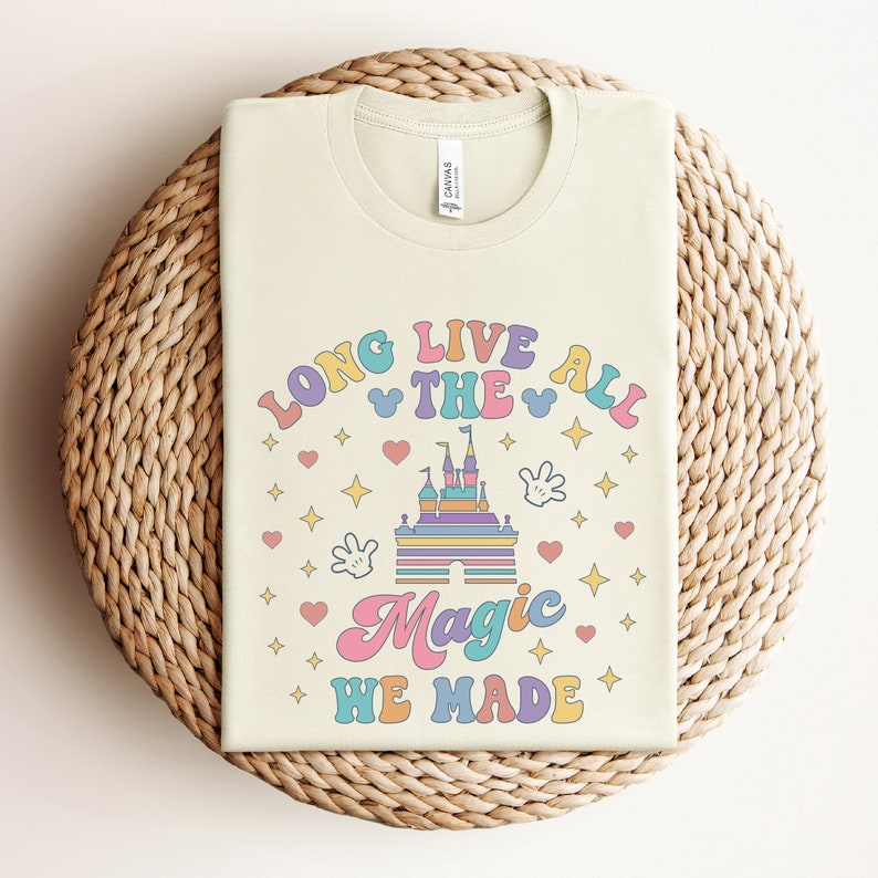 May include: A light beige t-shirt with a colorful graphic design that says "Long Live The All Magic We Made". The graphic includes a cartoon castle, stars, hearts, and Mickey Mouse ears.