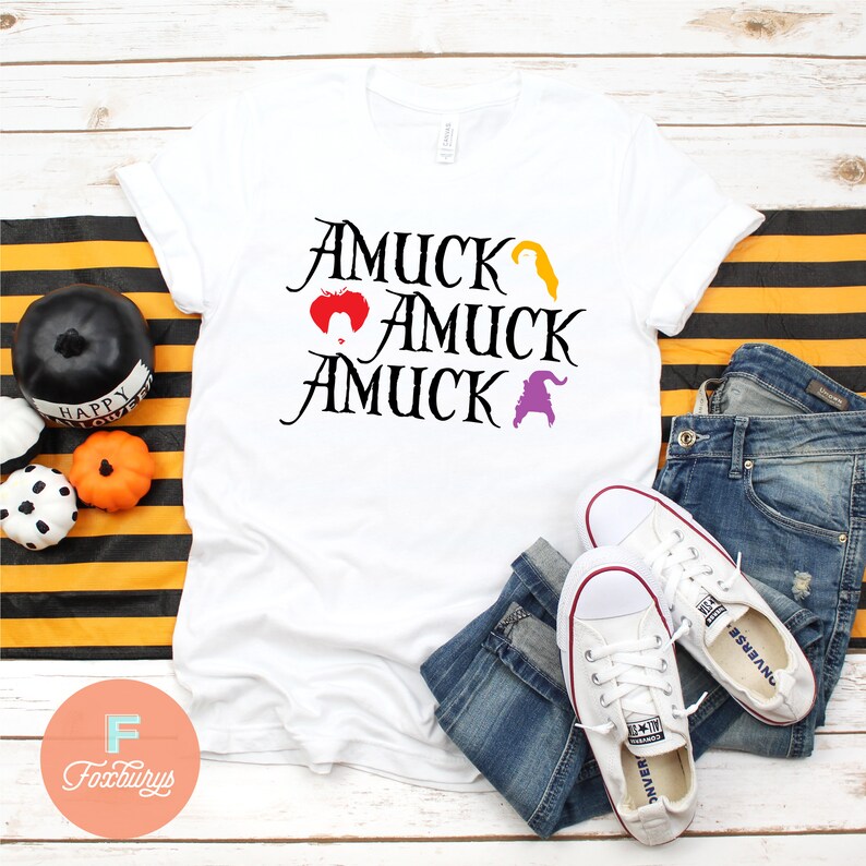 Puede incluir: Camiseta blanca con el texto "Amuuck Amuuck Amuuck" en negro. El texto est&aacute; apilado verticalmente. Hay tres peque&ntilde;as im&aacute;genes de brujas sobre el texto. La camiseta est&aacute; sobre una superficie rayada con un par de zapatillas blancas y unos vaqueros azules.